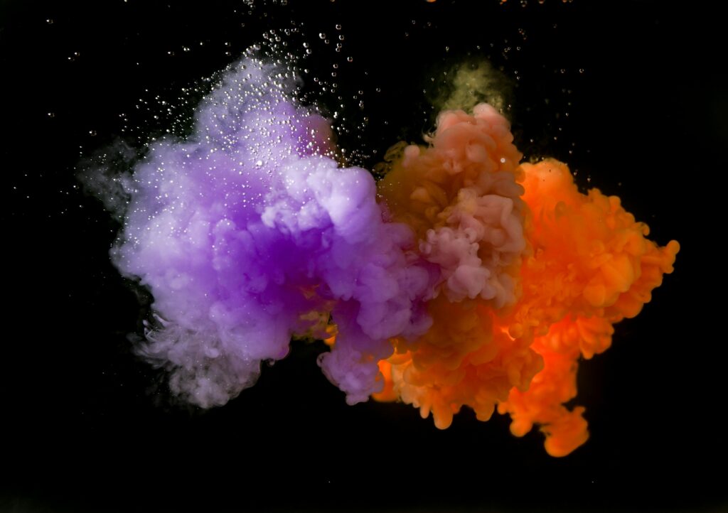 Dynamic fusion of orange and purple ink creating abstract art against a black background.